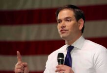 Rubio Drops Bomb On Biased Coverage man speaking with microphone in front of an American flag