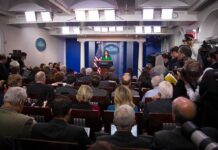 Press secretary at podium addressing reporters in briefing room