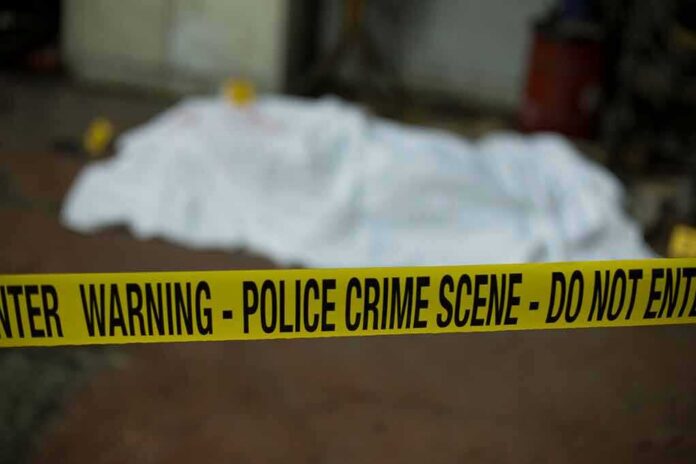 shutterstock_788116414 crime scene tape in foreground with covered body in background