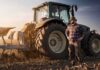 Farmer standing beside a tractor in a plowed field