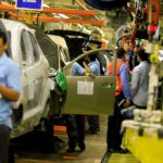 Trump Lands Audi Megaplant Bombshell Teddy Williams on an automotive assembly line with workers fitting car doors