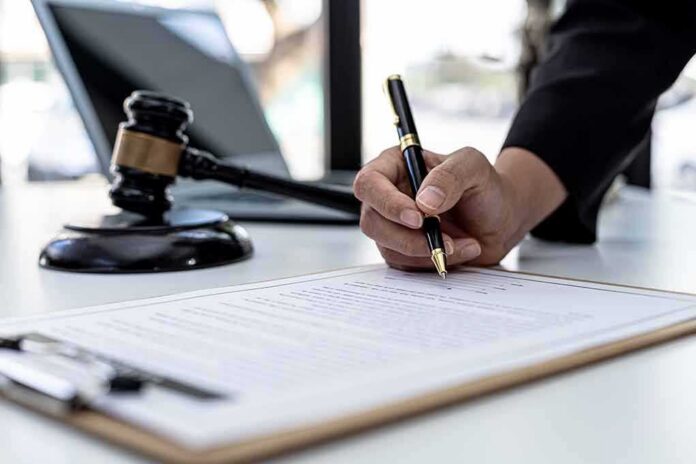 shutterstock_2103308165-1 Hand signing legal document beside gavel and laptop
