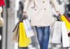 Person in beige coat carrying multiple shopping bags